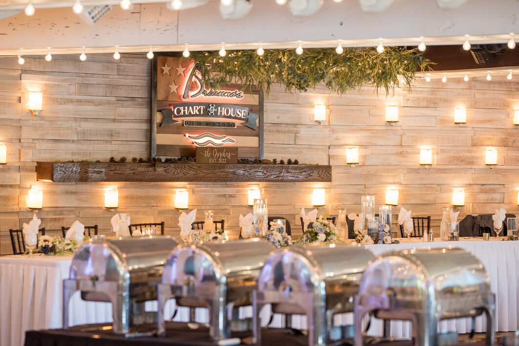 A buffet of chafing dishes set under string lights in front of the Chart House sign