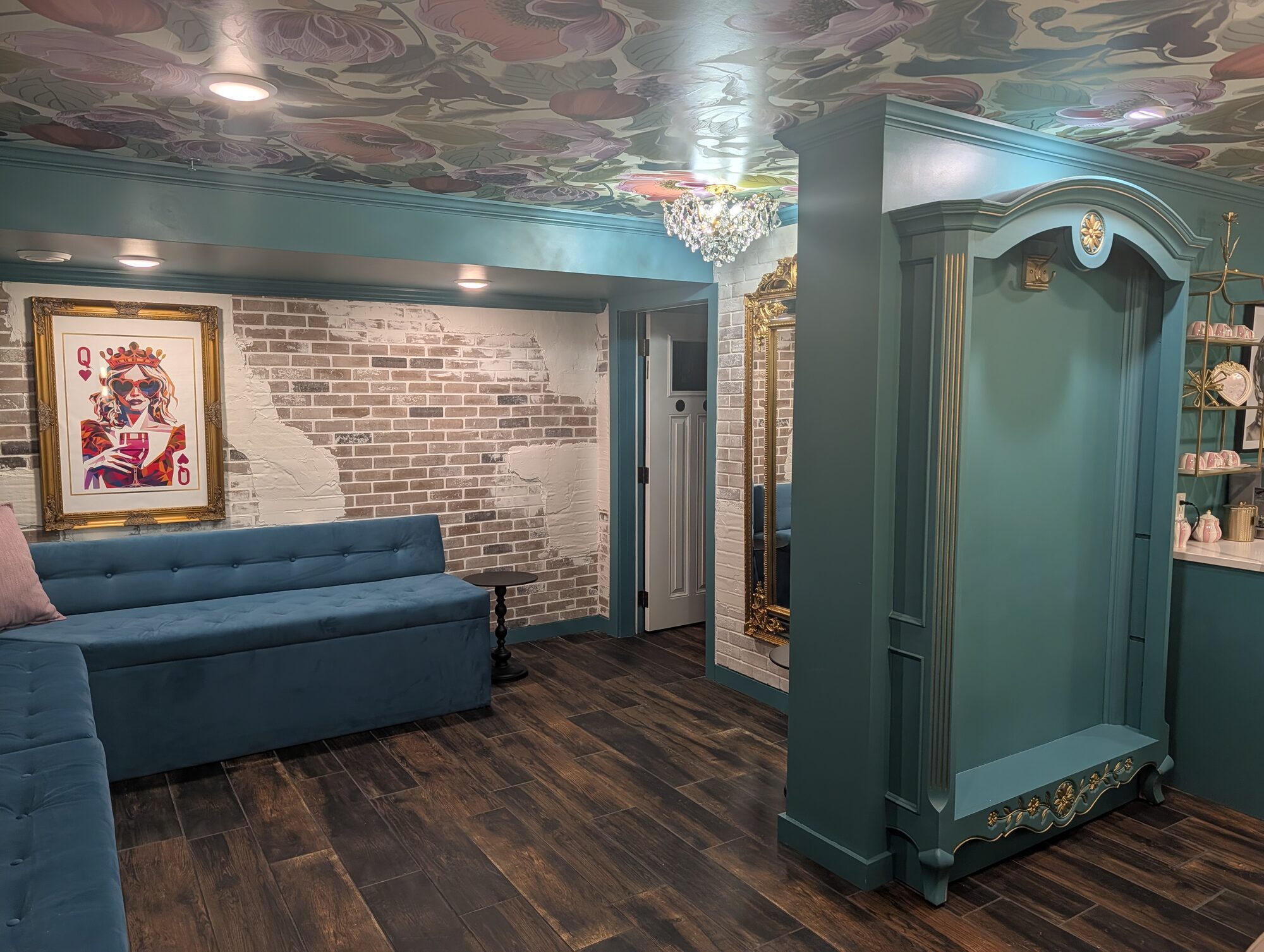 Bridal salon lounge with teal velvet seating, floral ceiling mural, and exposed brick at Glenhaven Events, Farmington MN