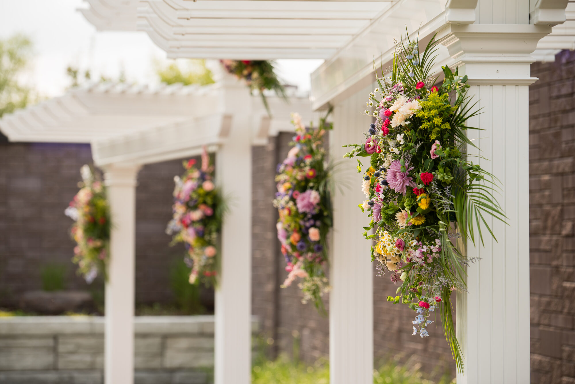 Lush wildflower arrangements in pink, yellow, and green mounted on the white pergola columns in the outdoor garden at Royal Cliff, Eagan MN